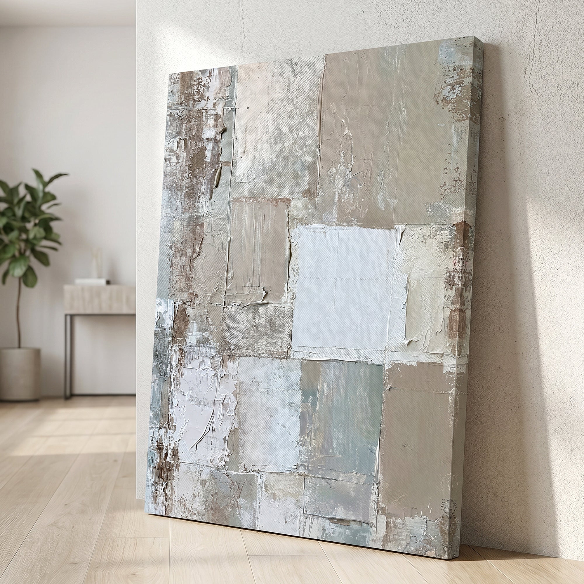 An abstract canvas wall art print with thick textured paint strokes in beige, gray, white, and muted blue-green, leaning against a textured off-white wall on a light wood floor.