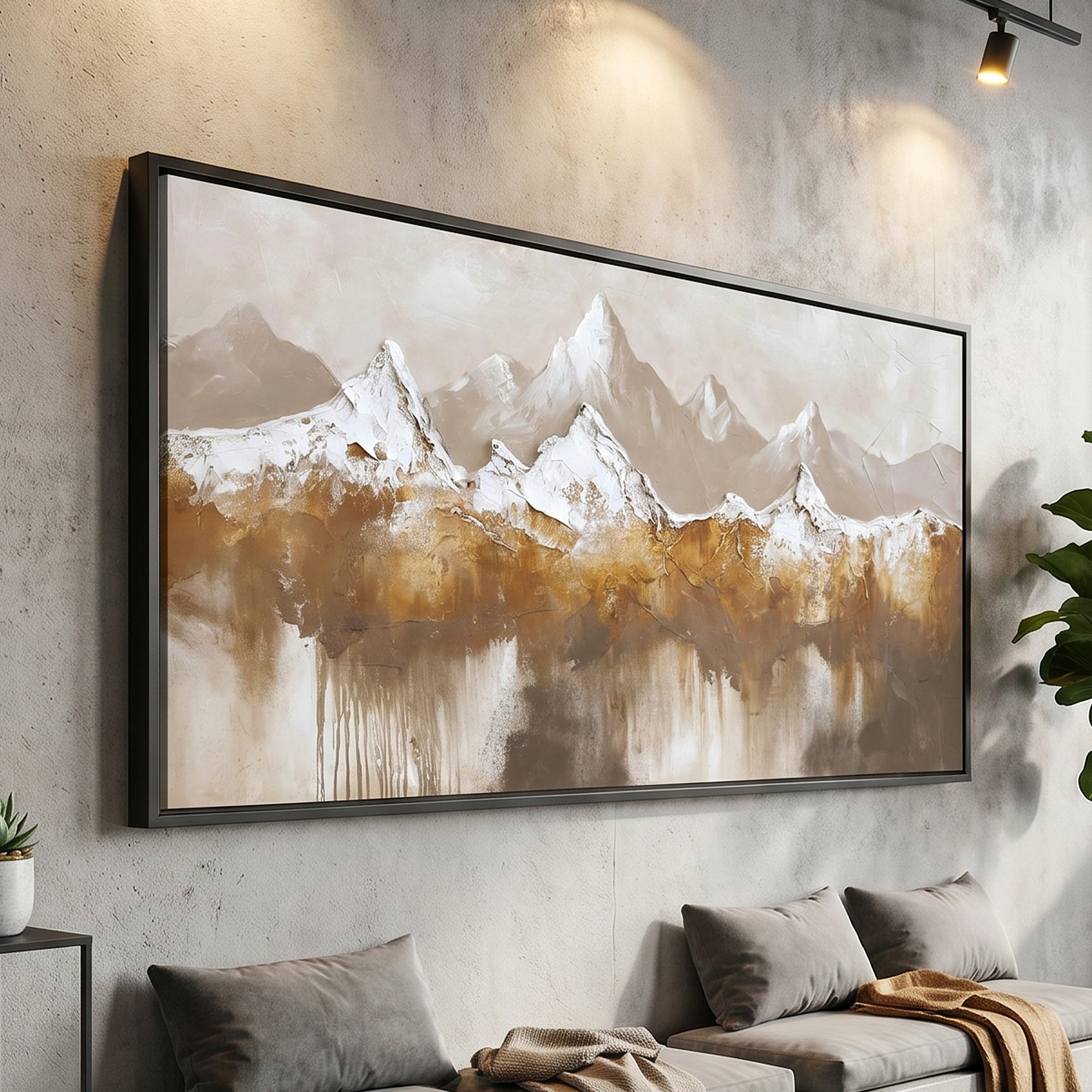 A large framed abstract mountain landscape wall art piece hangs on a textured gray wall above a sofa in a modern living room. The artwork depicts snow-capped peaks in white and beige with warm brown and gold washes below, set in a black frame.