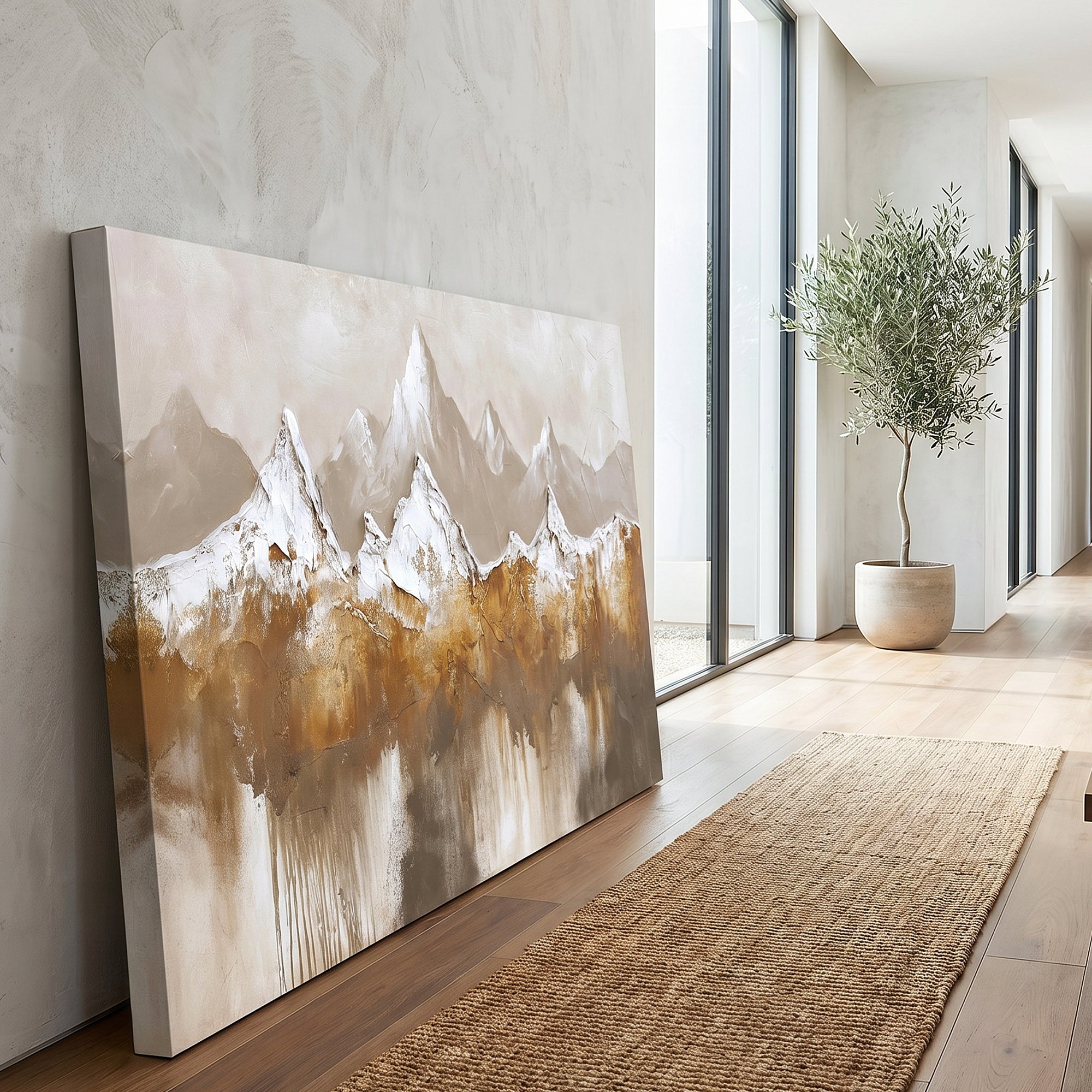 Large rectangular canvas wall art leaning against a light wall in a modern interior hallway. The artwork depicts stylized mountain peaks in white, beige, gray, and warm brown tones.