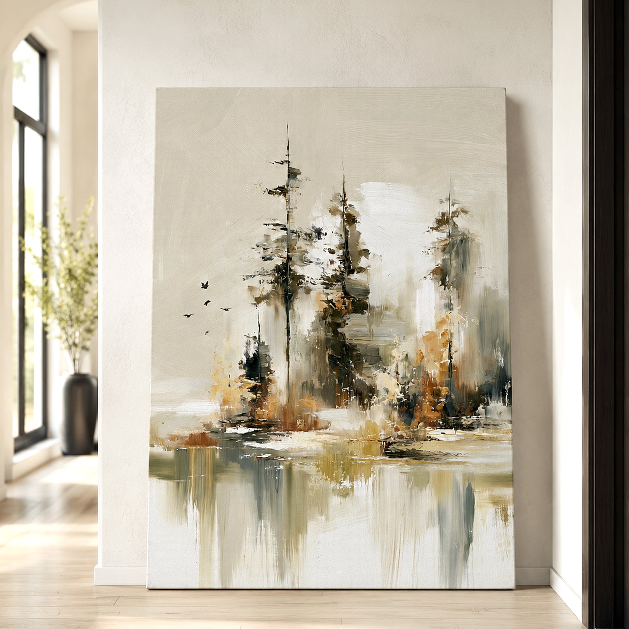 Abstract canvas wall art featuring three stylized trees in black, gray, white, and warm brown tones, displayed leaning against a light beige wall in a modern interior setting.