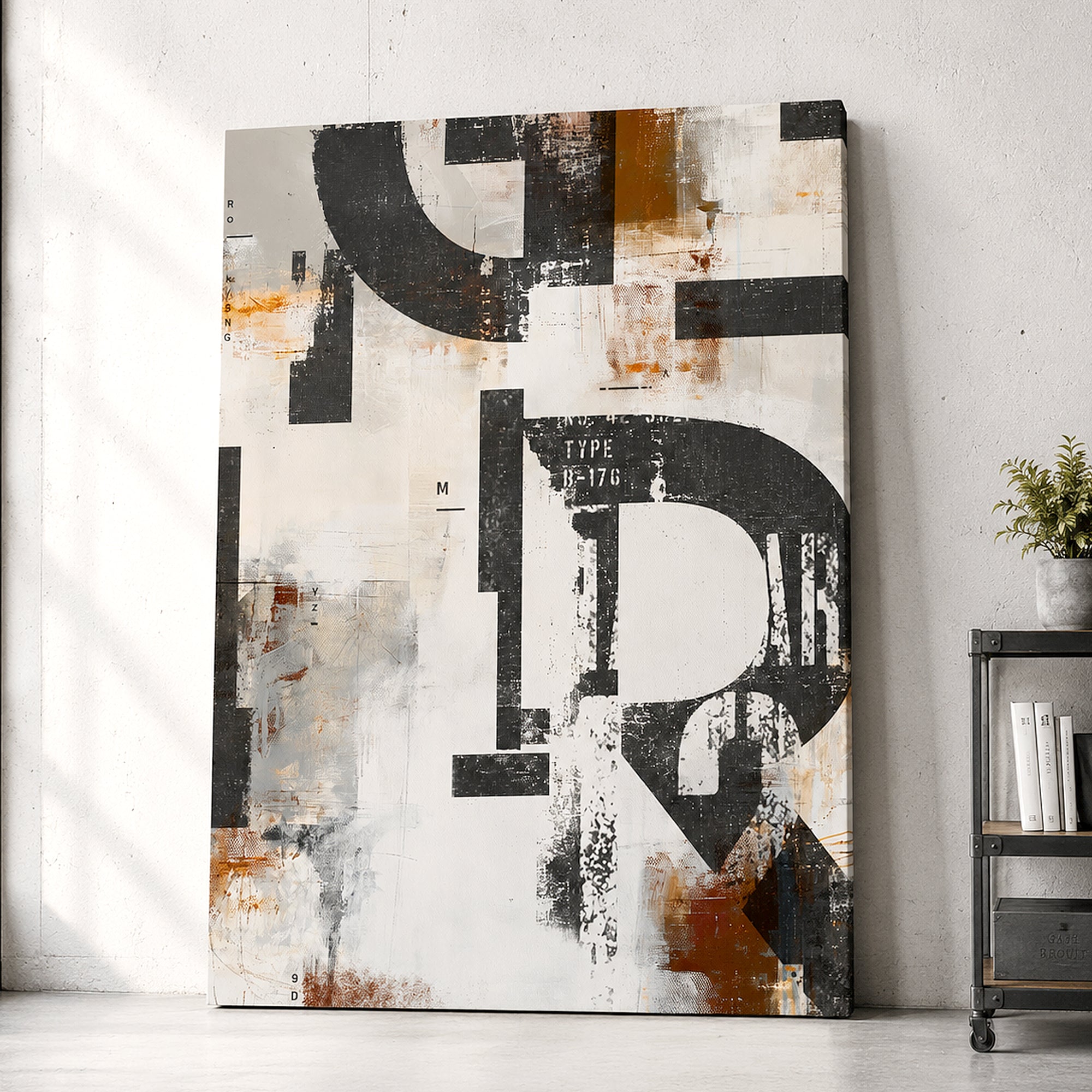 Abstract canvas wall art leaning against a light gray concrete wall in a styled interior setting, featuring large black letters and distressed textures in black, white, gray, and rust orange.