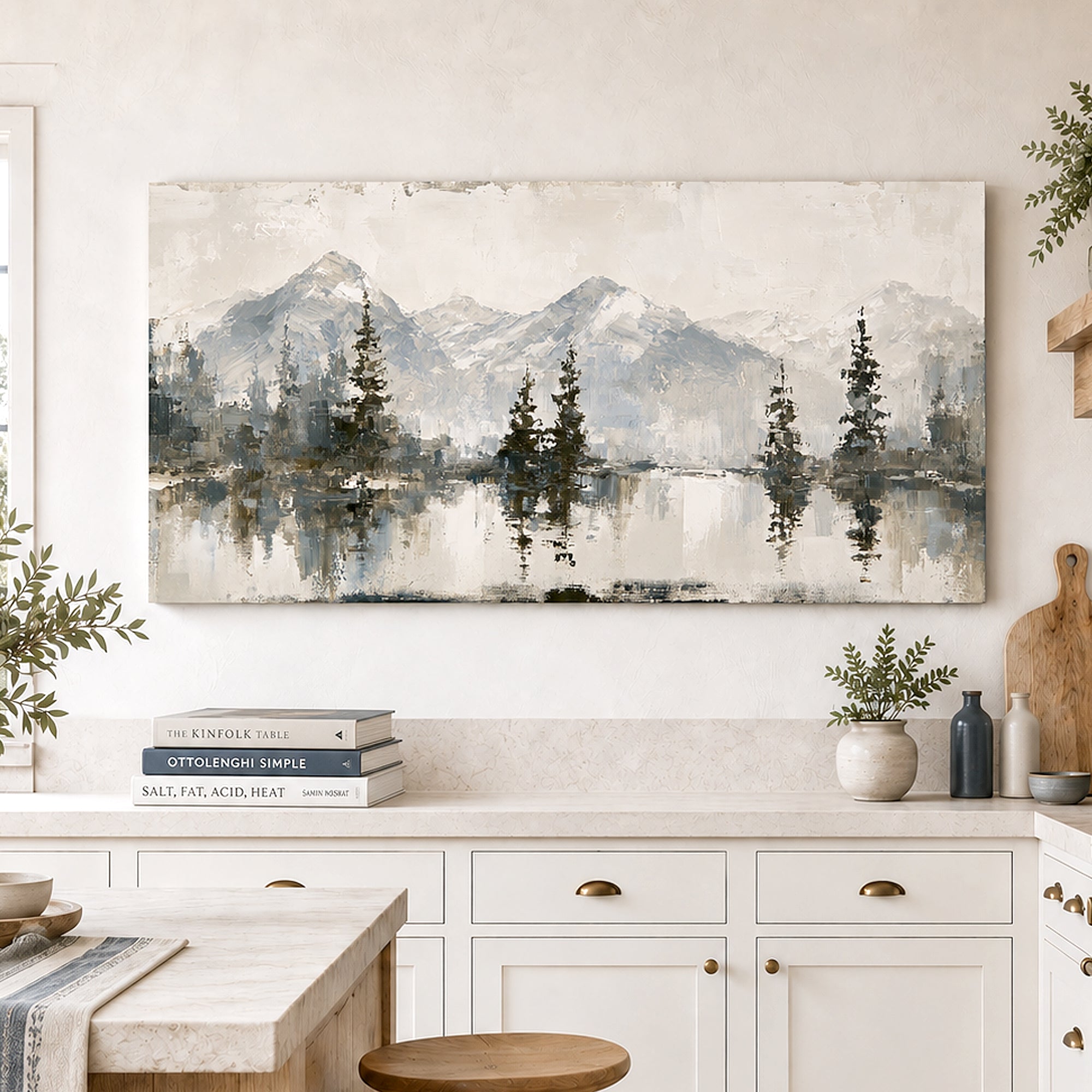 A large rectangular canvas wall art print depicting a misty mountain lake landscape with pine trees, hung on a light wall above a white kitchen counter in a styled interior.