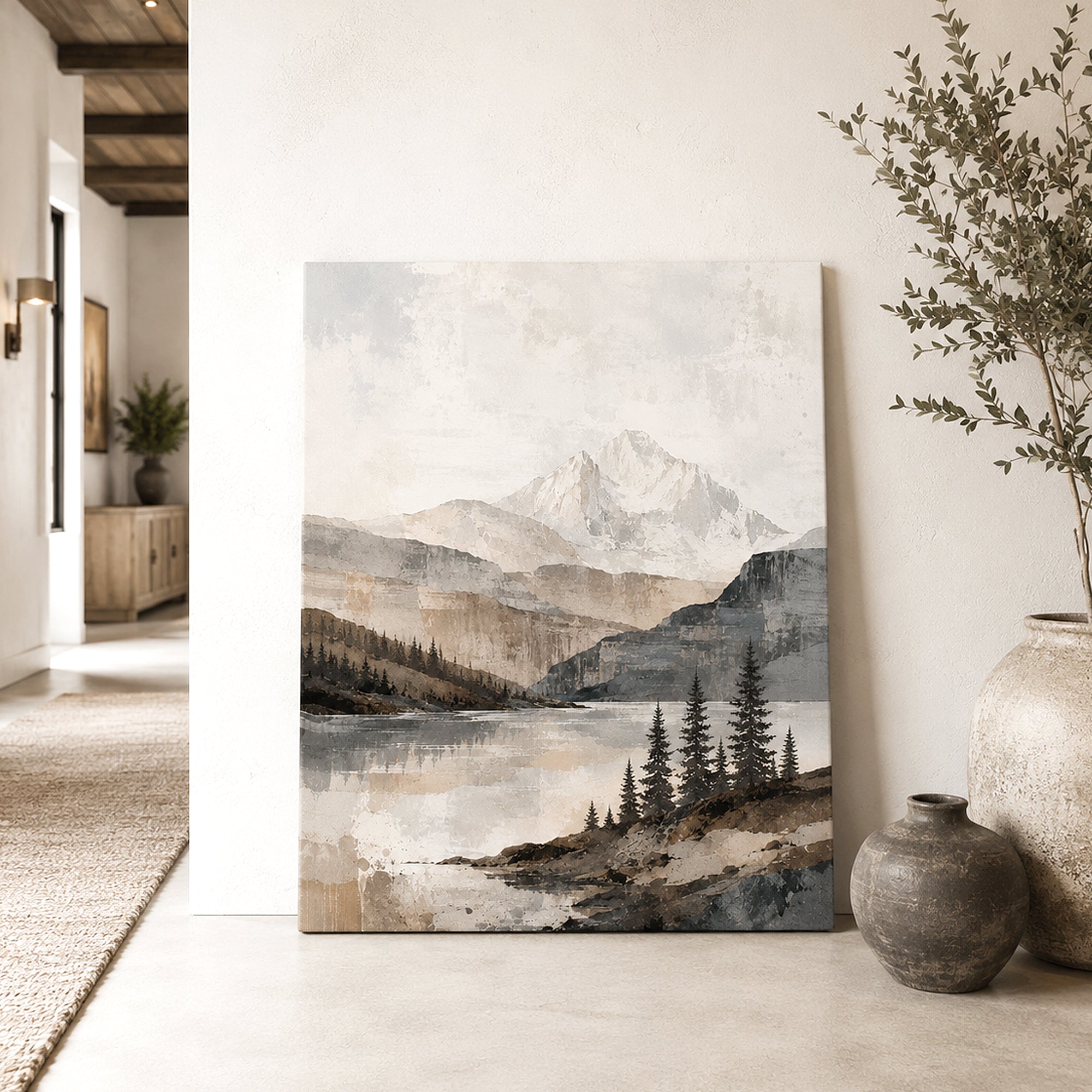A vertical canvas print of a serene mountain lake landscape, styled leaning against a white wall in a modern, sunlit room alongside decorative ceramic vases and a dried plant.