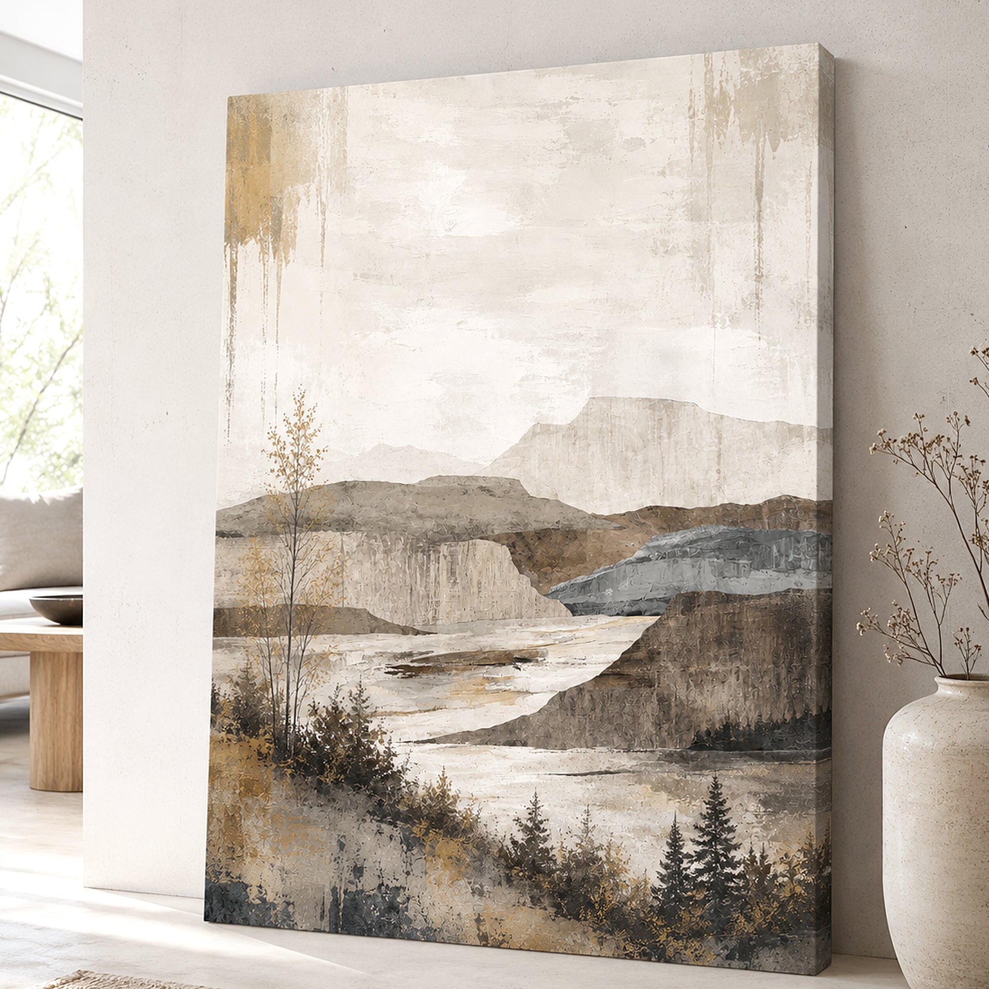 A vertical canvas wall art print featuring an abstract landscape with mountains, water, and trees in muted beige, brown, gray, and blue tones, displayed leaning against a light wall in a styled interior setting.