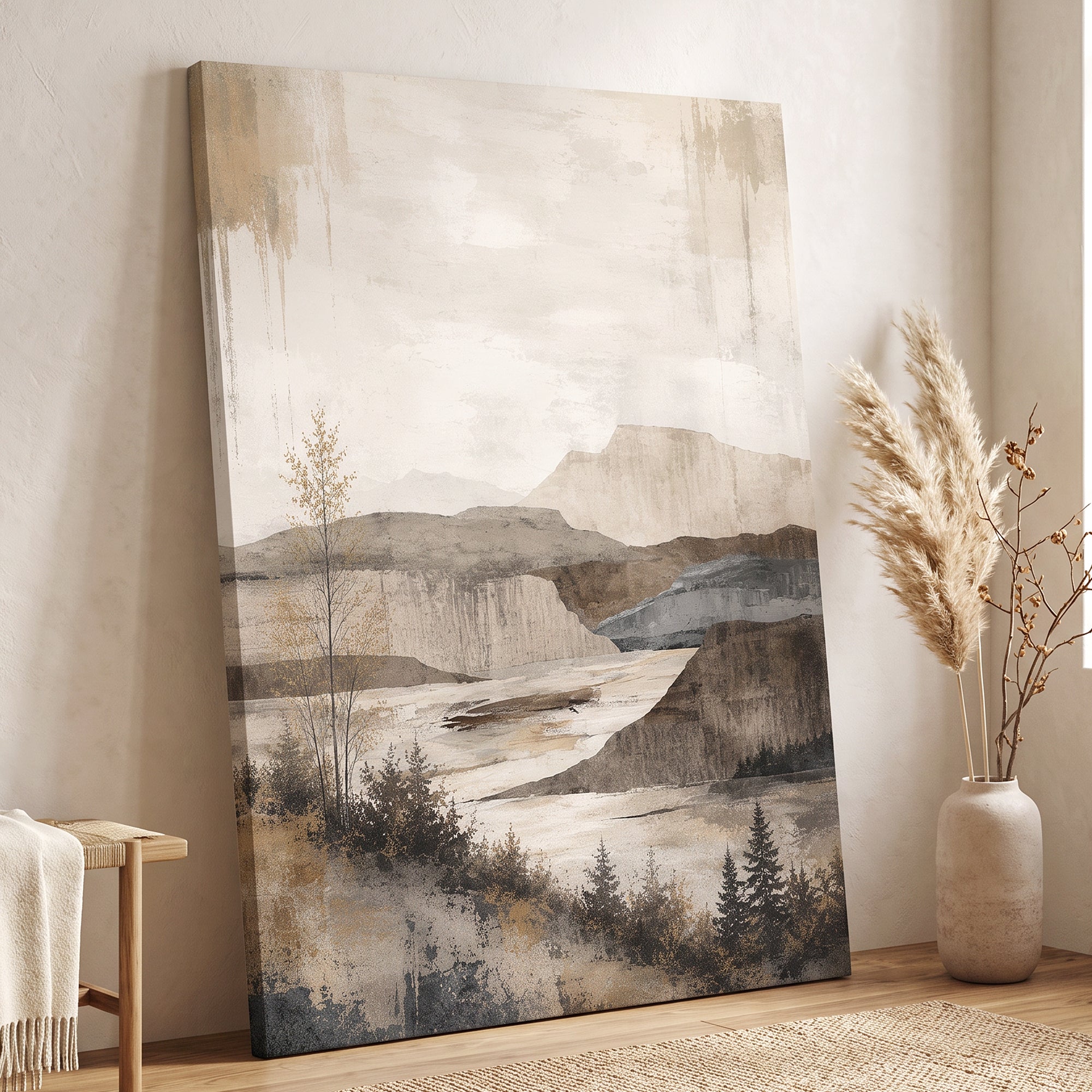 A large vertical canvas print featuring a muted landscape painting with mountains, trees, and a river, styled in a warm, neutral-toned room next to a wooden bench and a vase of dried pampas grass.